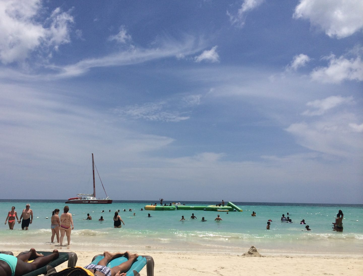 People sunbathing and water inflatables, swimmers and a boat in the water at 7 Mile Beach