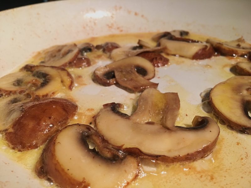 Sauteeing mushrooms in a white frying pan
