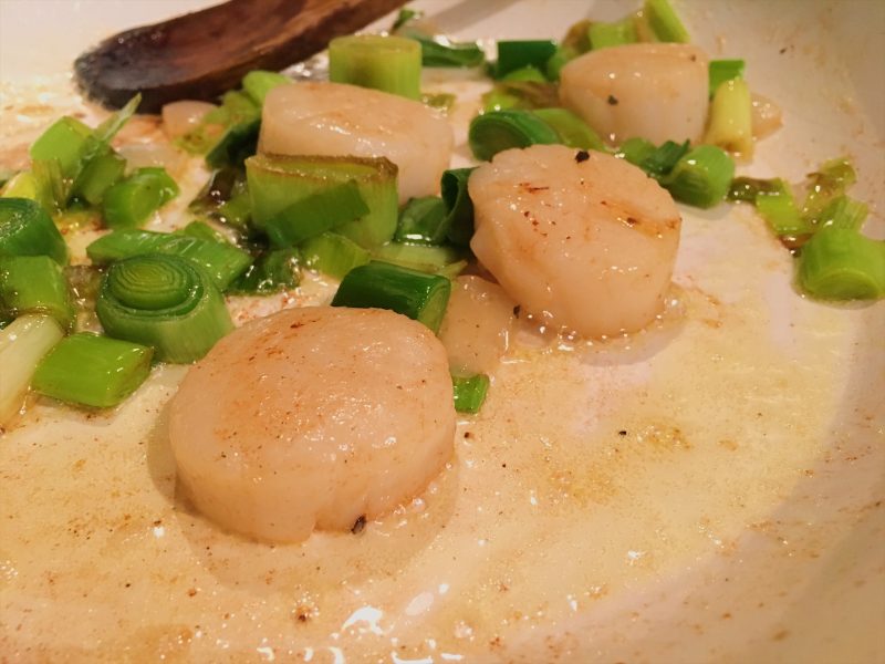 Scallops and leeks cooking in a frying pan
