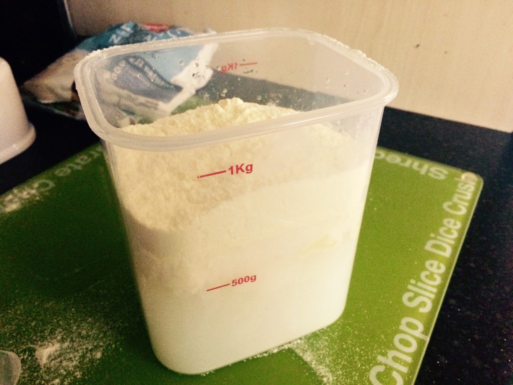 A plastic tub filled with water and yoghurt mix, not yet stirred