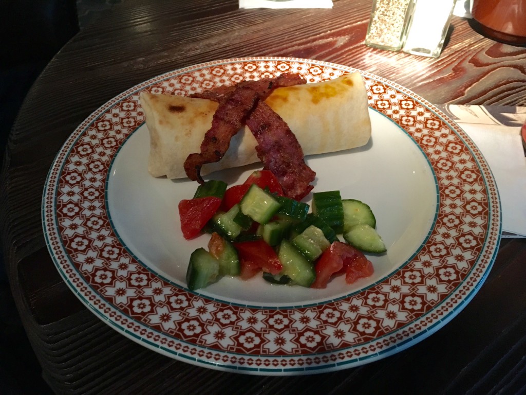 A breakfast burrito topped with crispy bacon rashers and served with chopped cucumber and tomato