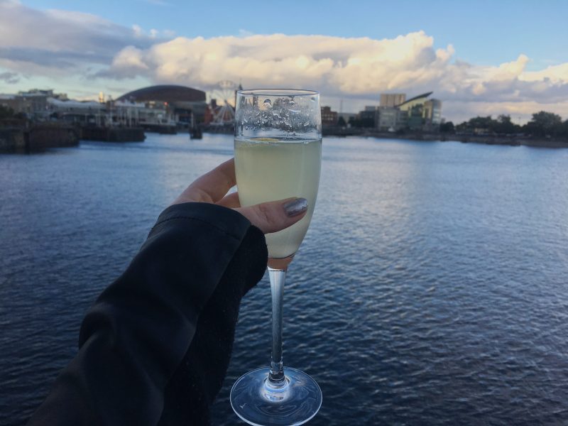 Holding a glass of Prosecco against the backdrop of Cardiff Bay