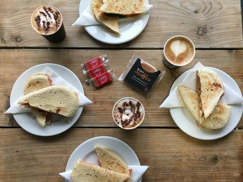 A flatlay of paninis, hot drinks, Lotus biscuits and Tregroes toffee waffles at Blue Lagoon Cafe at Bluestone Wales