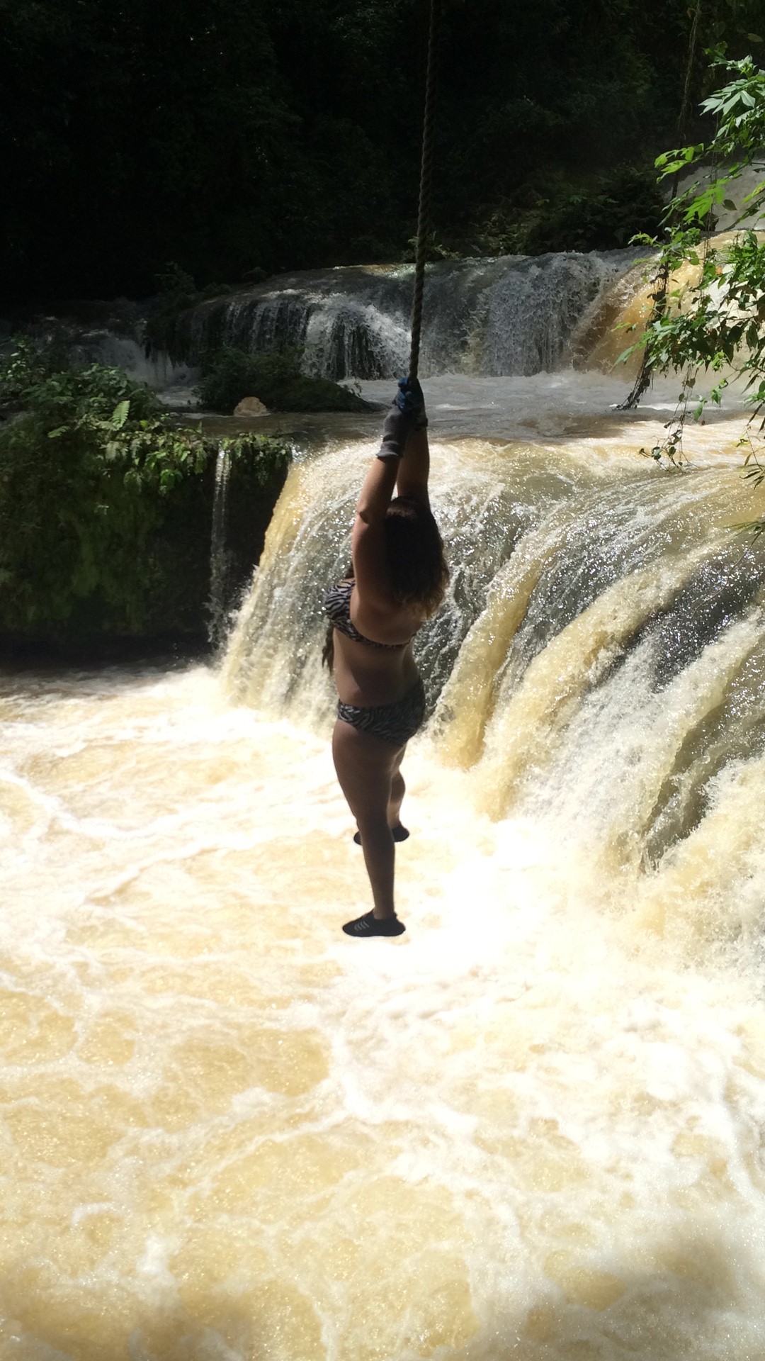 Jumping off a rope swing into a waterfall at YS Falls, Jamaica