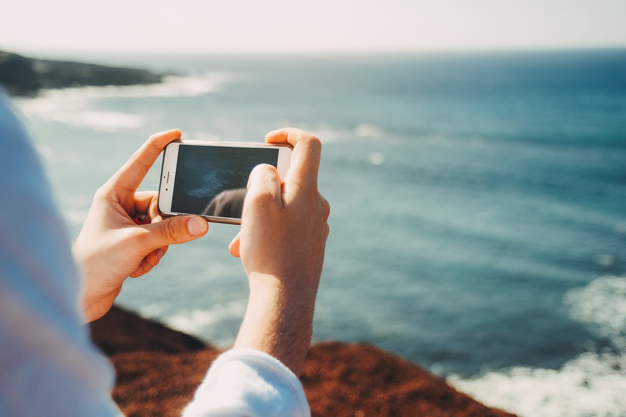 Hand holding mobile phone, taking a photo of the sea