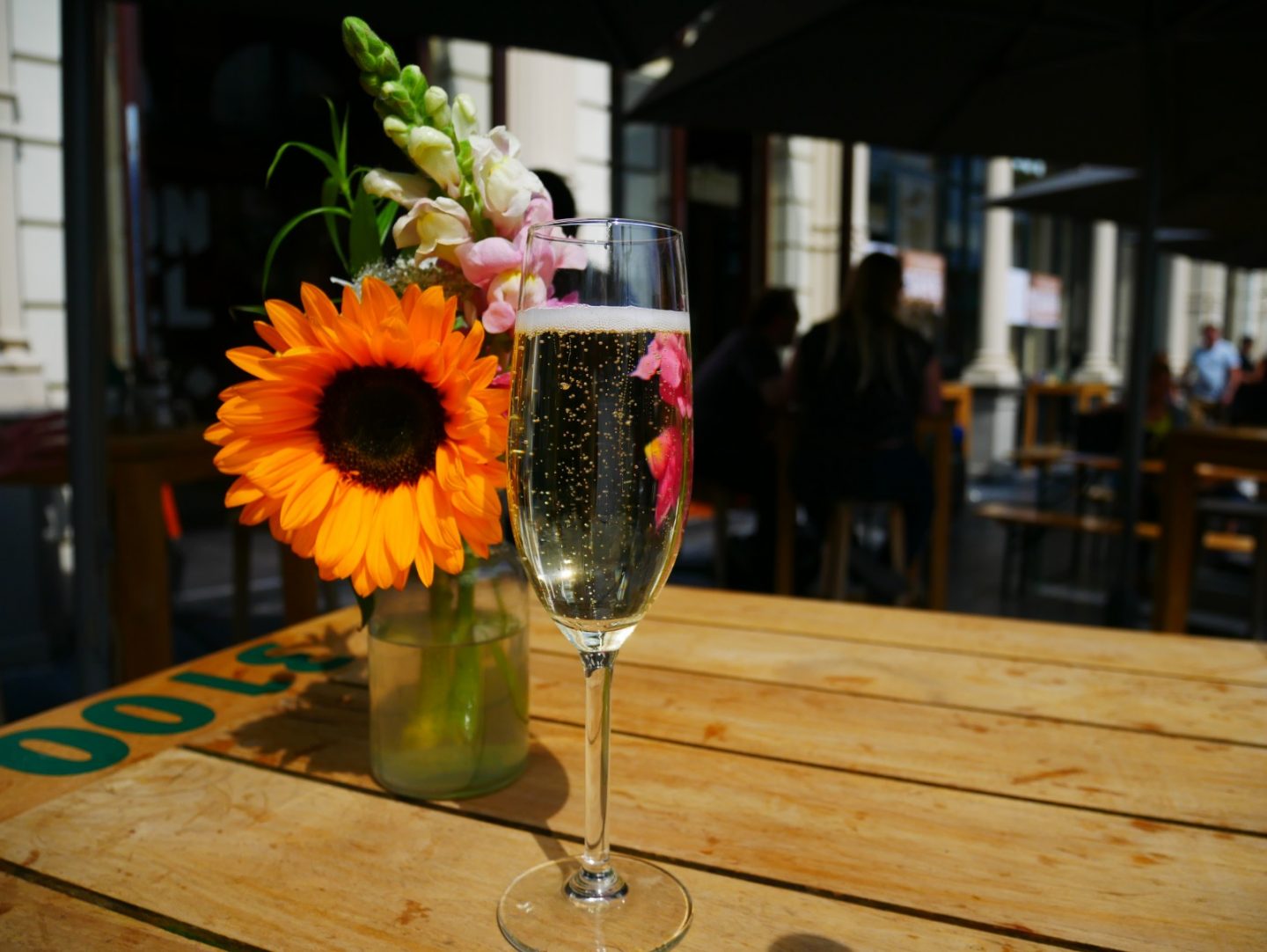A glass of Prosecco standing next to a sunflower arranged in a vase.