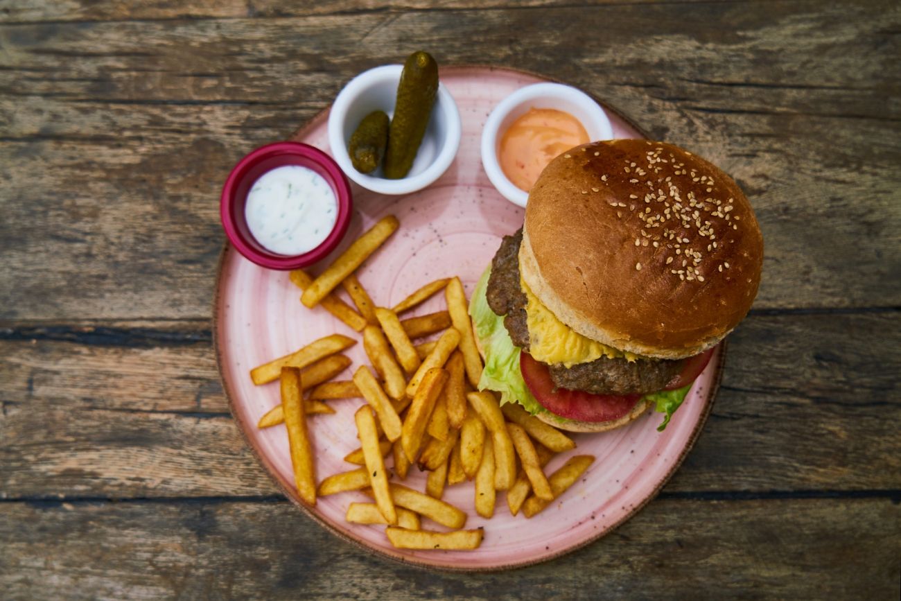 A plate holding a cheeseburger, golden fries, pickles and dips.
