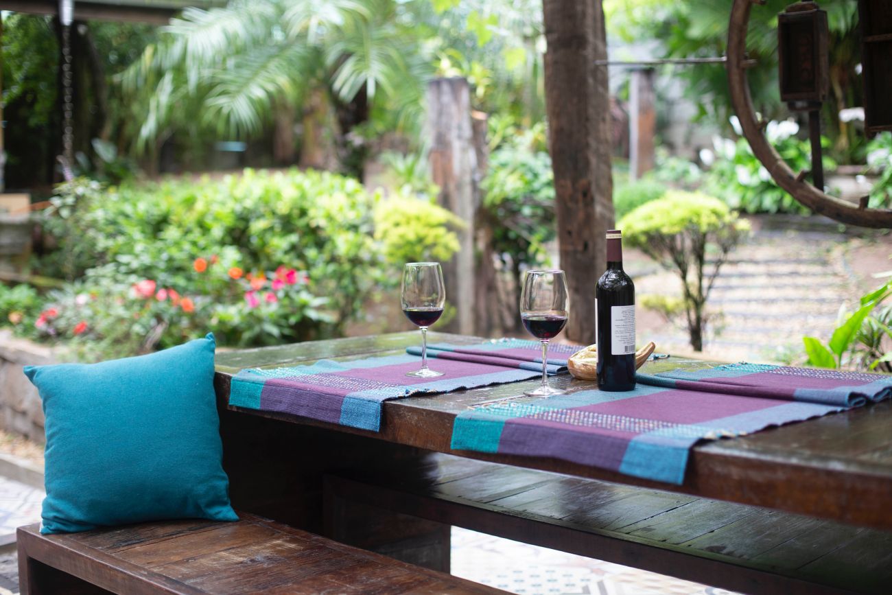 A garden table topped with a bottle of wine and two glasses of wine.
