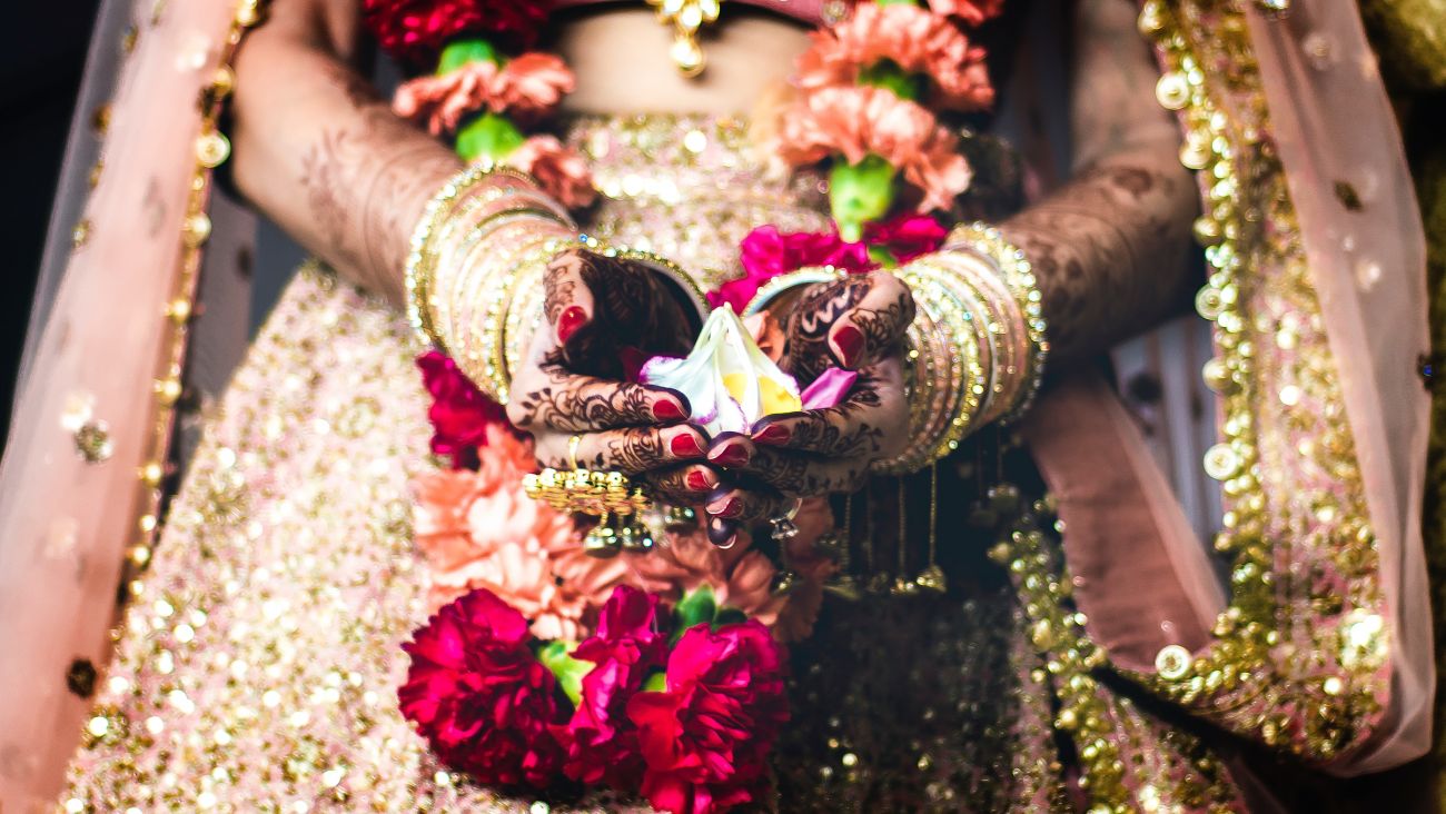 An Indian bride wearing a heavily embellished dress, folding flower petals in her henna-decorated hands.