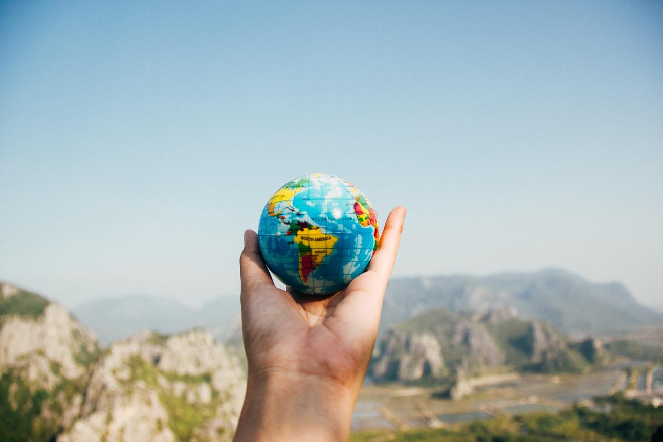 A hand holding a small globe, with rocky mountains in the distance.