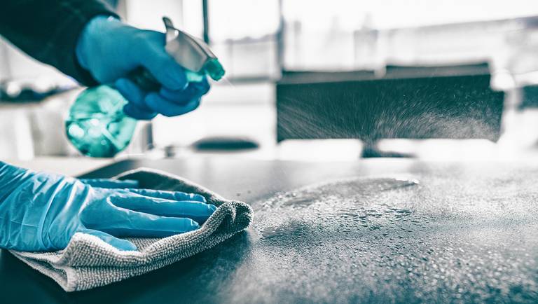 Hands wearing disposable gloves, wiping a work surface and spraying cleaning solution.