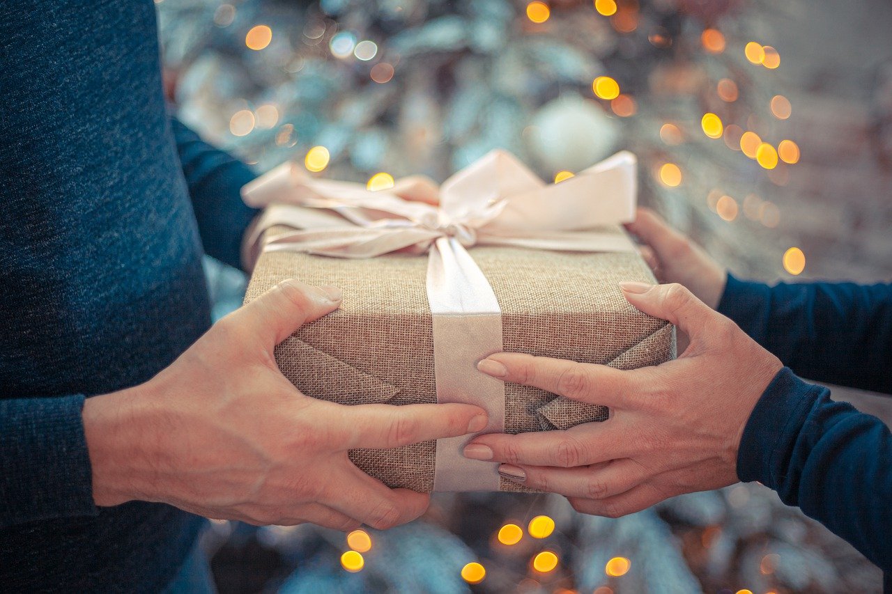 Hands exchanging a gift wrapped in brown cloth with a white ribbon