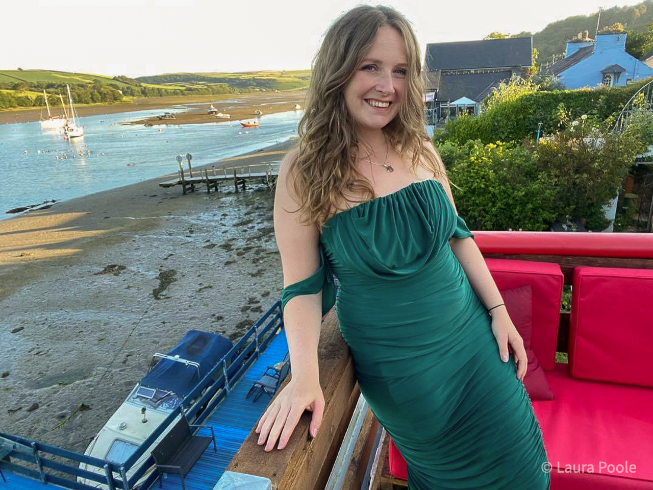 A lady wearing an emerald green dress at the seaside, leaning on a fence.