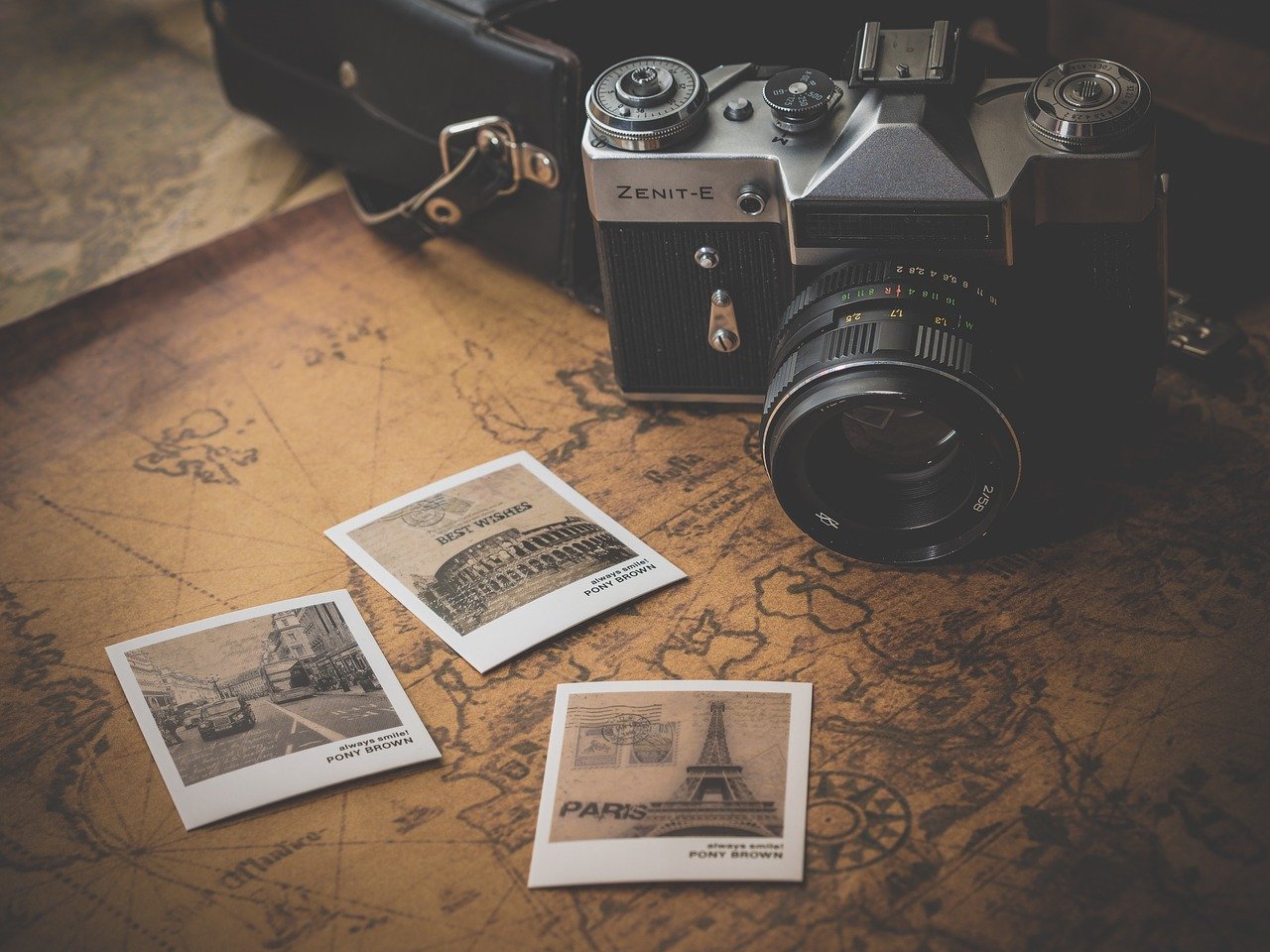 An old camera sitting on a map, next to some Polaroid photos