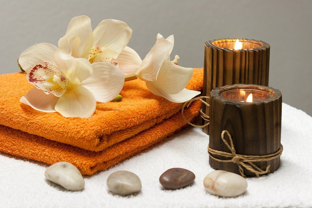 An orange towel, flowers, candles and stones in a spa setting