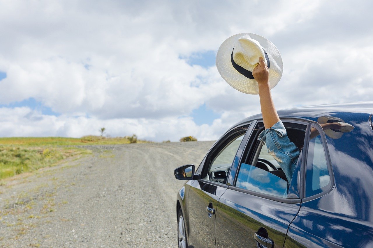 A man waving a straw hat out of the window of a car