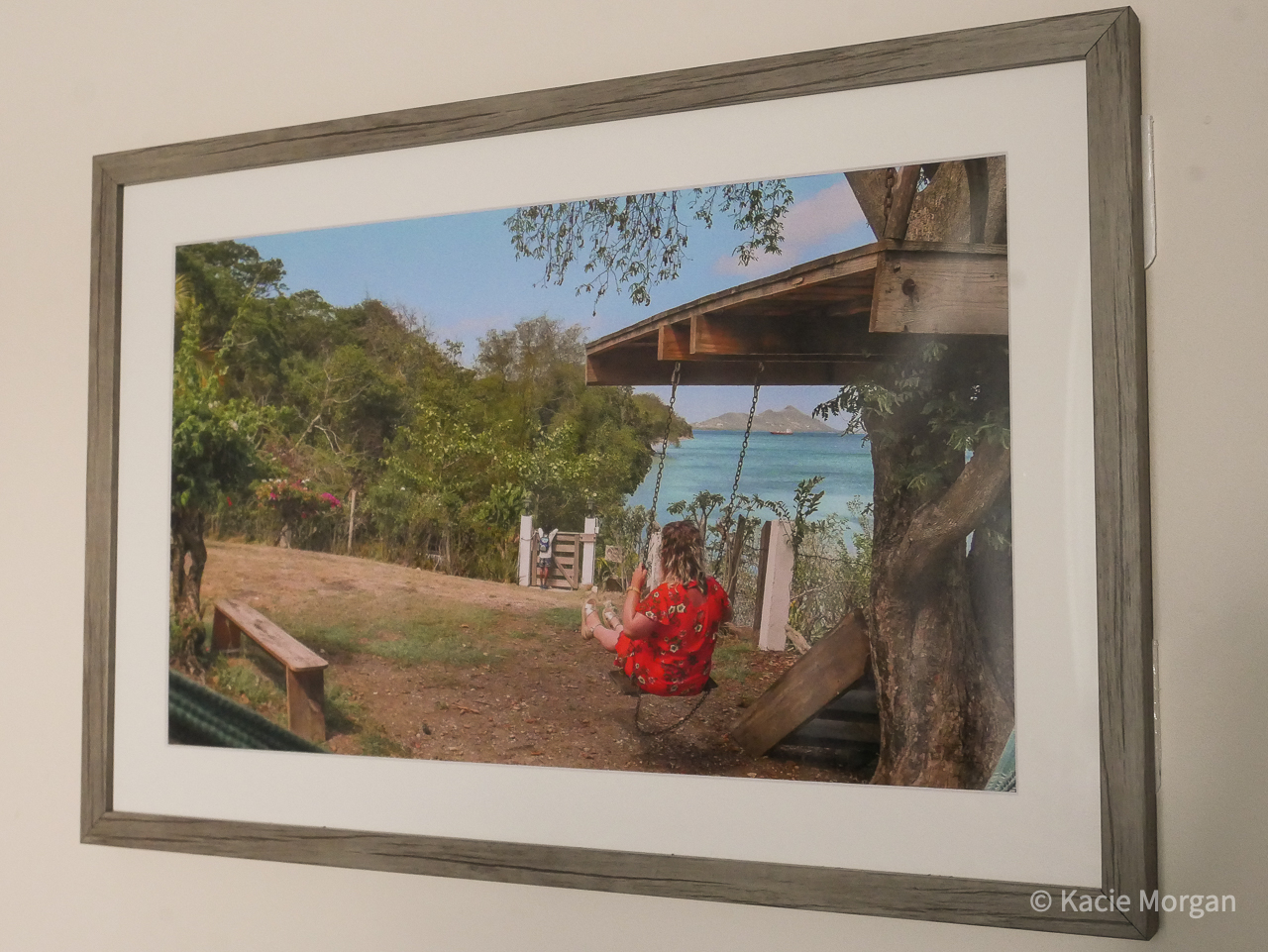 A photo of a girl on a swing overlooking the Caribbean Sea, placed inside a frame hanging on a wall.