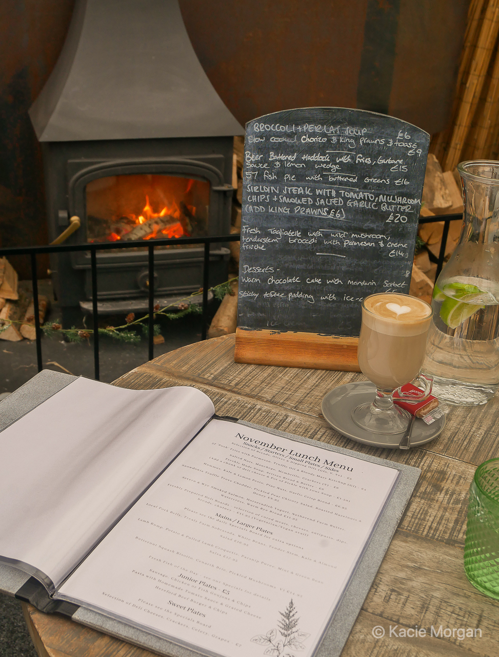 A menu and latte sitting on a table in front of a log burner
