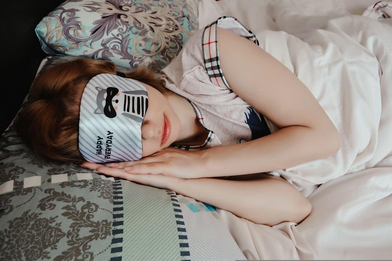 A lady sleeping in bed, wearing an eye mask.