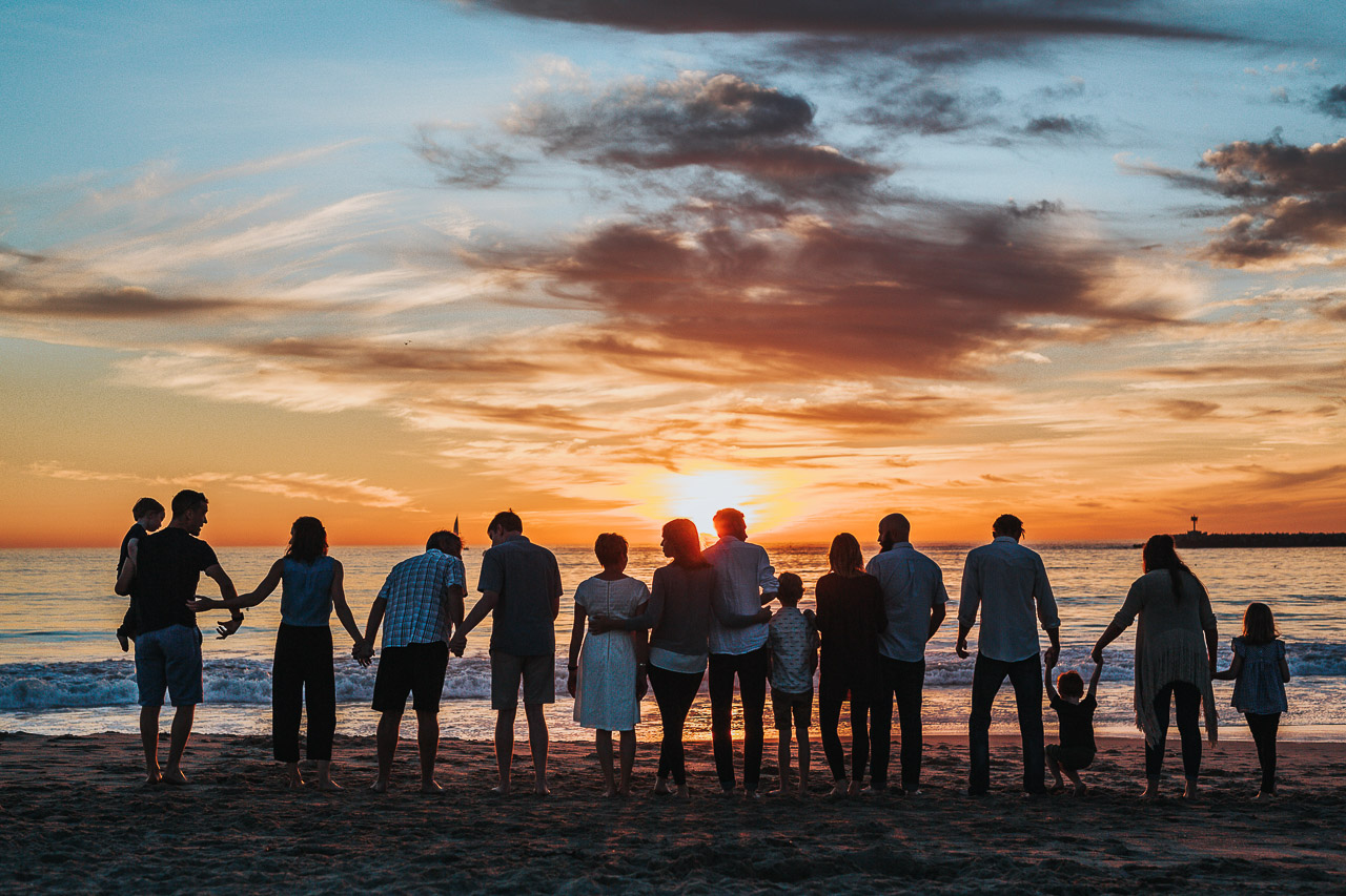 A group family travel shot - lot of people holding hands and/or with arms around each other, on the beach