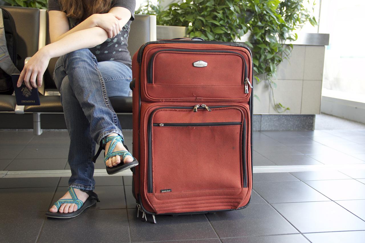 A lady sitting next to a red suitcase in an airport, holding a passport.
