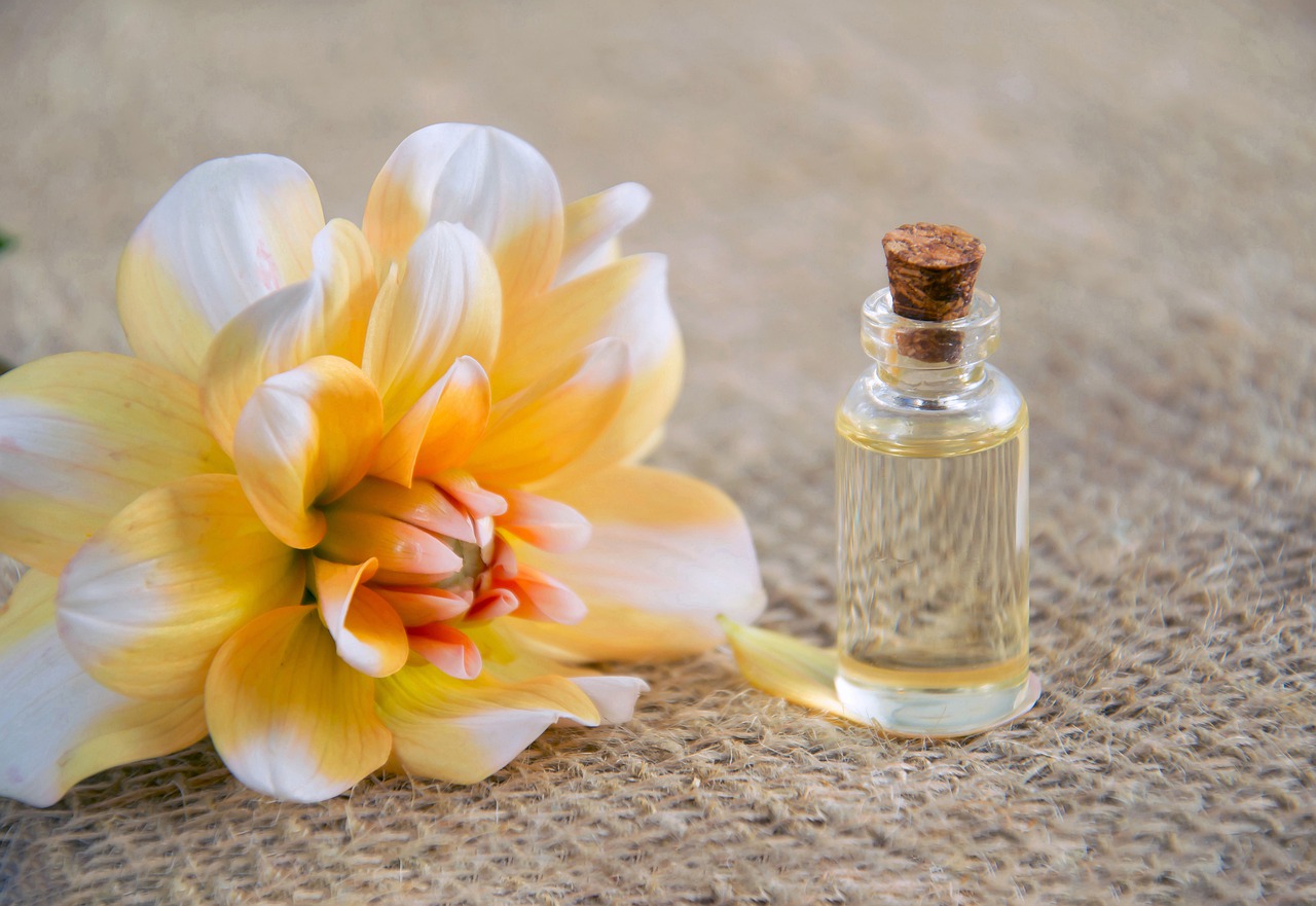 An orange/white flower next to a small bottle of body oil.