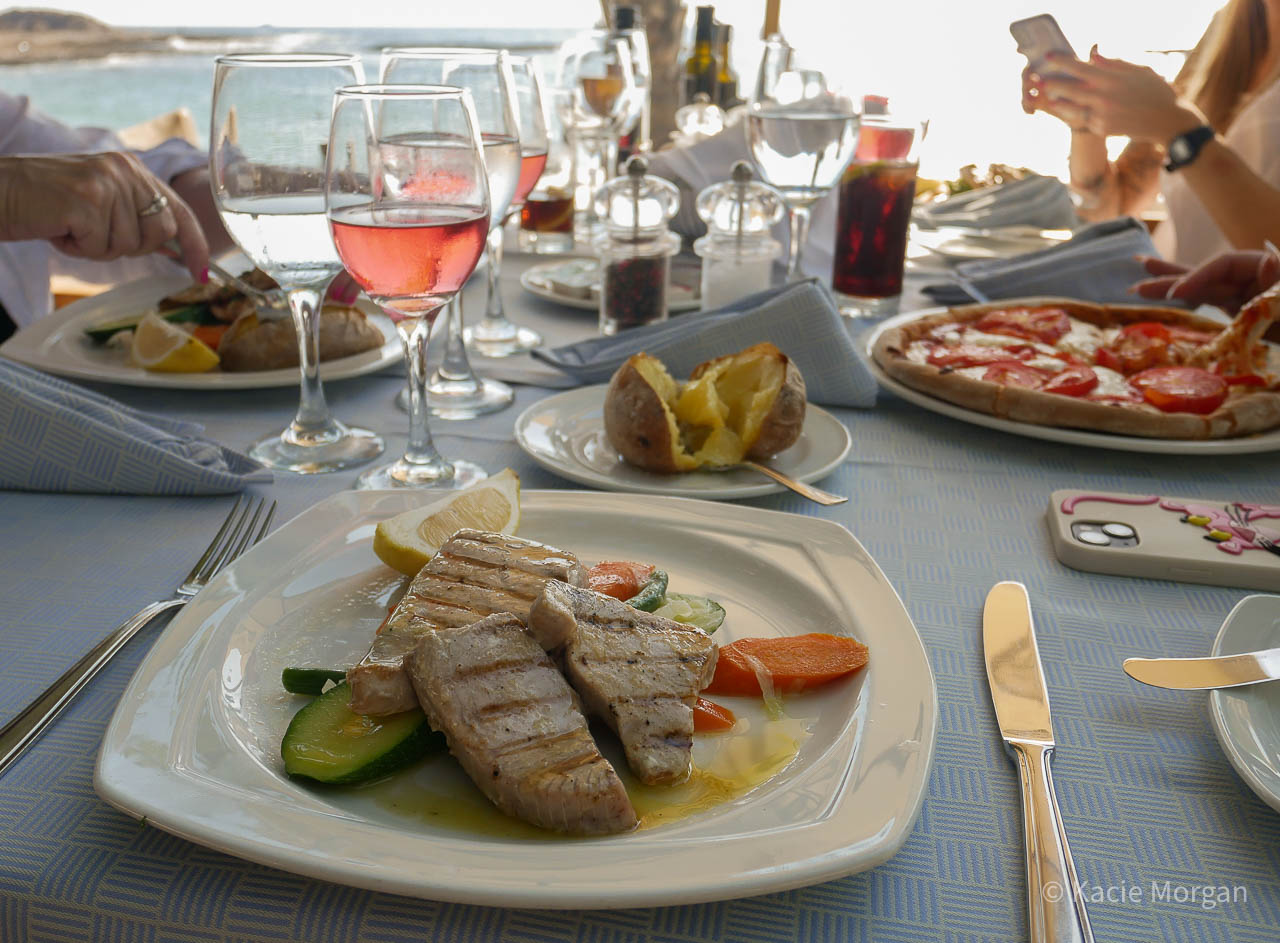 Fresh grilled tuna with veg and a jacket potato, on a dining table where others are also eating