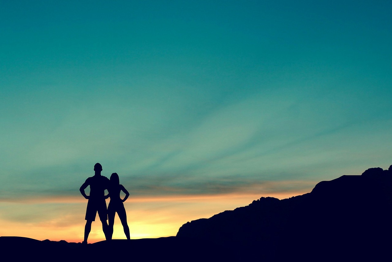 The silhouettes of a couple standing at the top of a mountain.