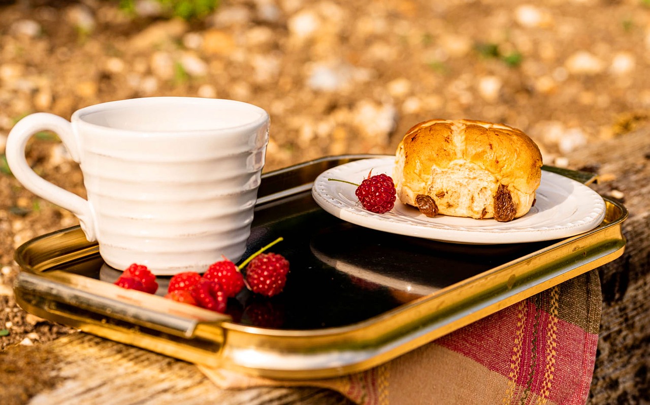 Hot cross bun and a cup on a tray, with some raspberries