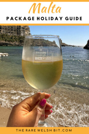 Wine glass filled with white wine, bearing the words 'Malta Gozo', photographed on Xlendi Bay in Gozo, Malta