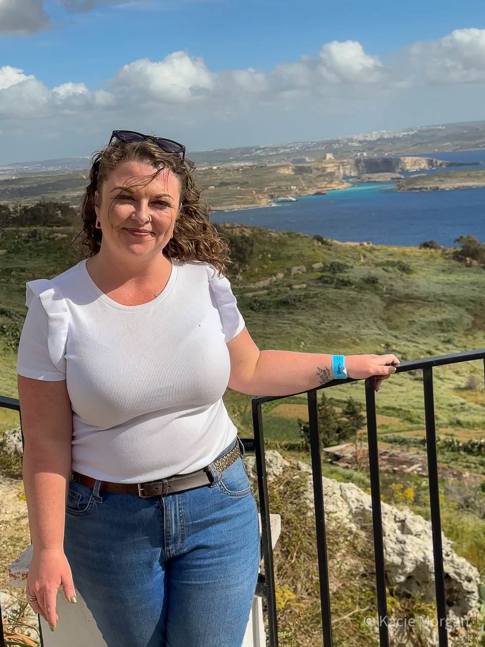 Me standing next to a railing overlooking Comino island and its beautiful Blue Lagoon, while on holiday in Malta