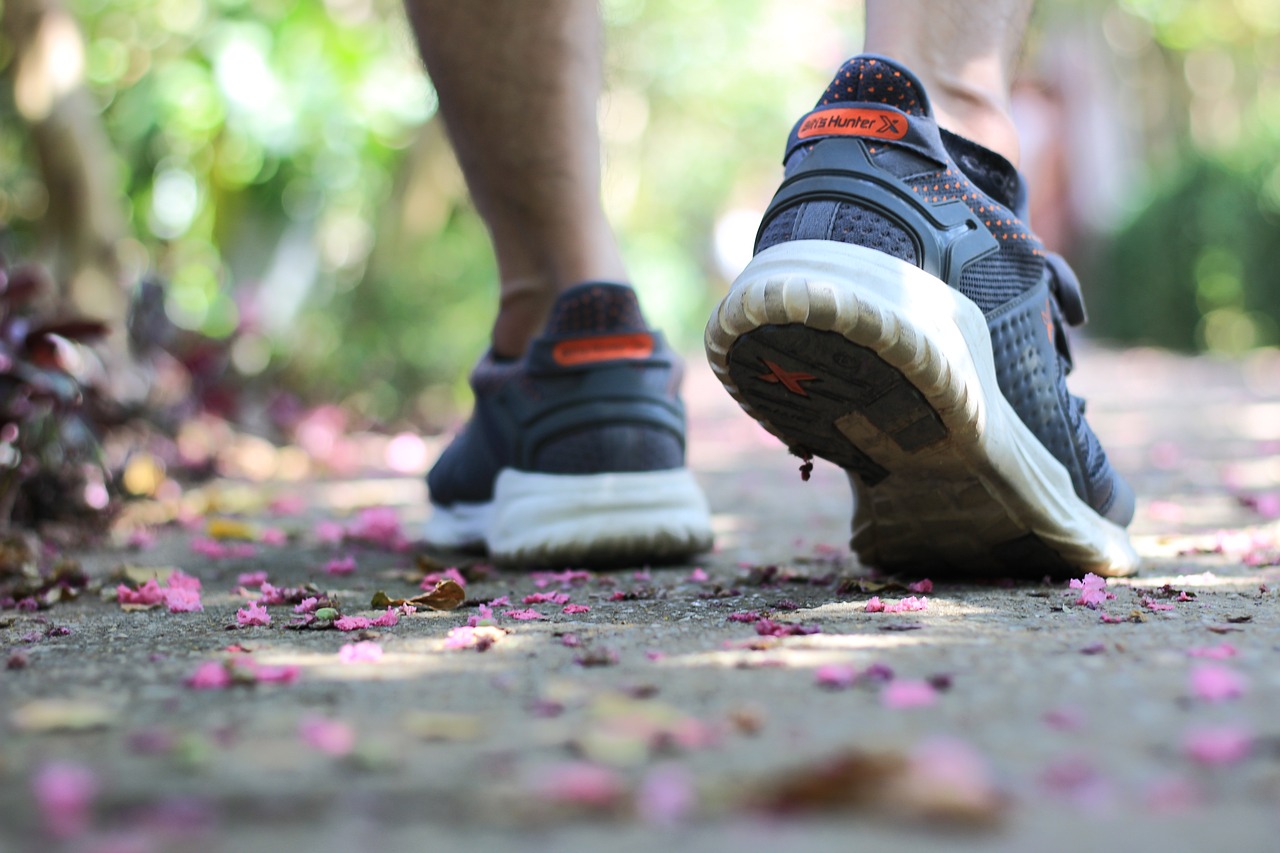 A man wearing a pair of trainers, walking down a petal-strewn path, photographed from behind.