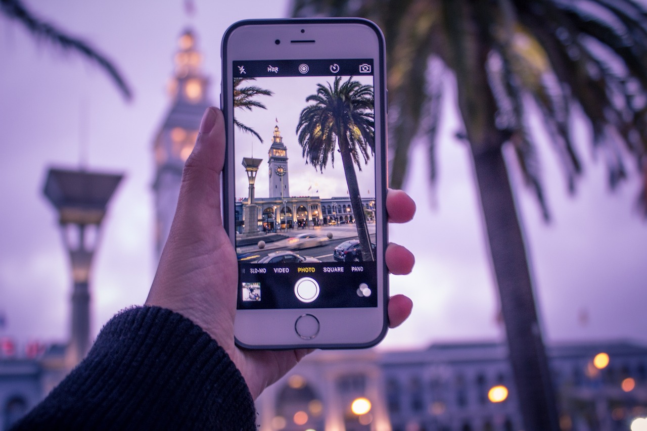 A hand holding a smartphone, taking a photo of a landmark.