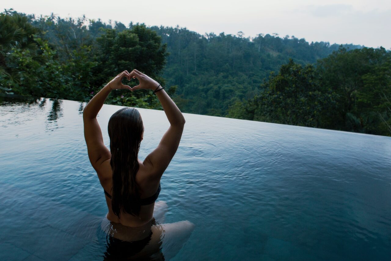 A female in a swimming pool, making a heart shape using her hands