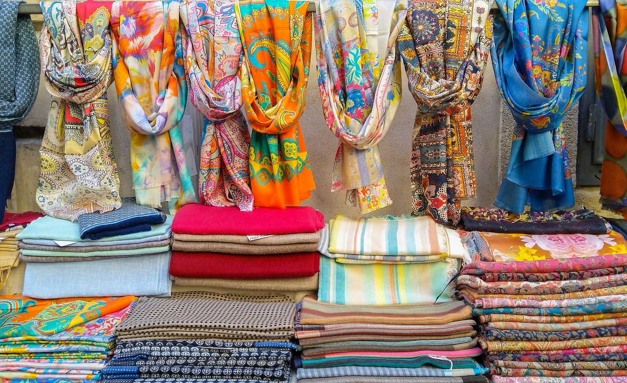 Colourful folded scarfs, with more scarfs hanging overhead, on a clothing stall.