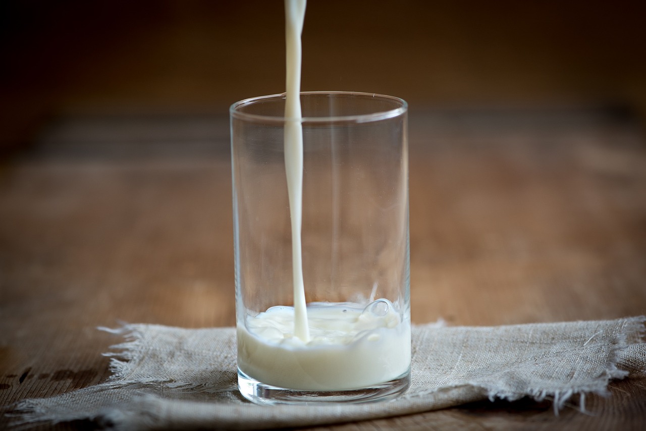 A glass sitting on a beige fabric square on a wooden table, with milk being poured into it.