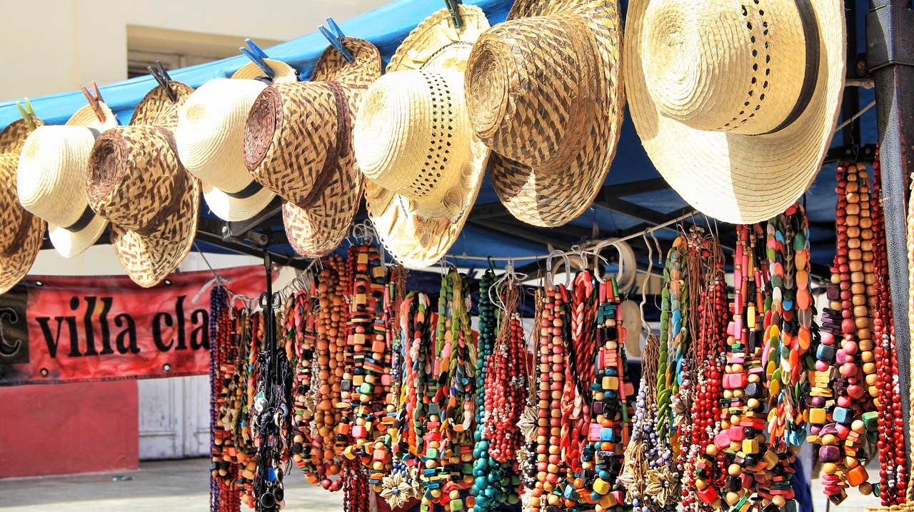 Colourful beaded necklaces hanging on a rail, with rimmed straw hats hanging overhead.