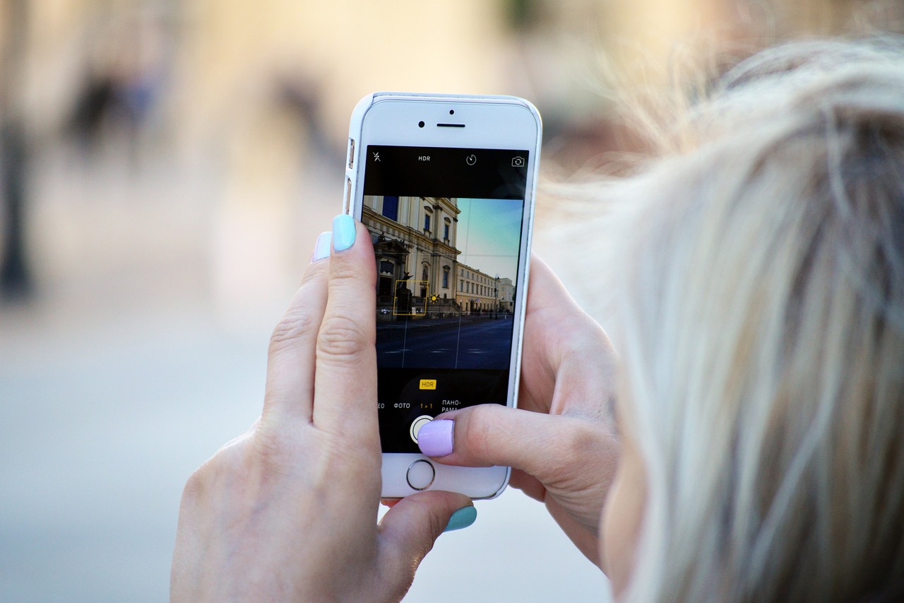 A gitl with blonde hair photographed close up from behind, taking a photo of a building on her iPhone while adjusting the HDR settings.