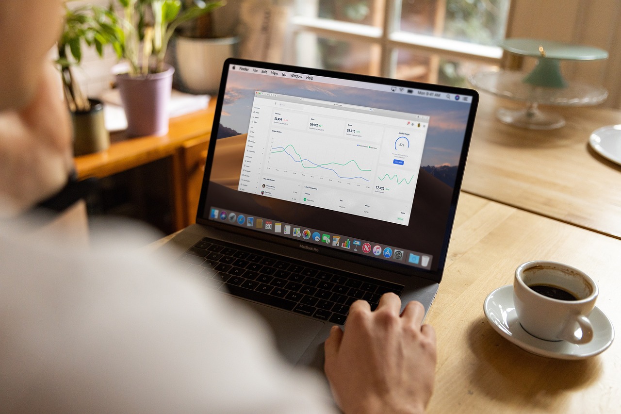 Someone photographed from behind using a laptop, with a cup of coffee next to them.