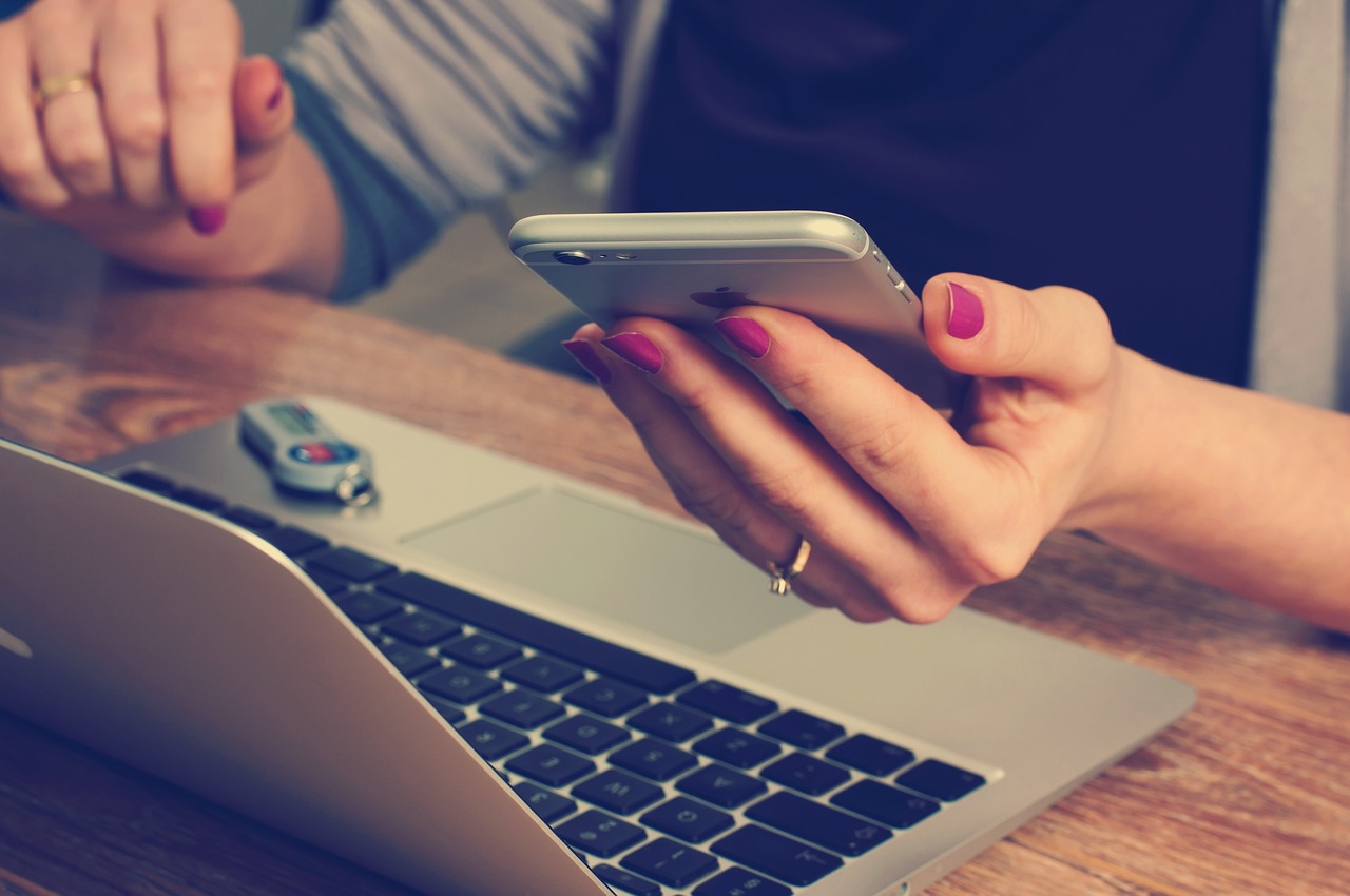 A lady's hand holding a smartphone, while browsing on a MacBook.