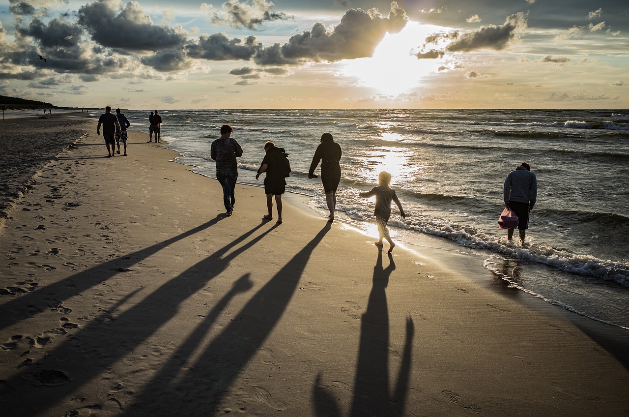 People walking along a golden sandy beach, following the coastline, with their shadows cast behind them.