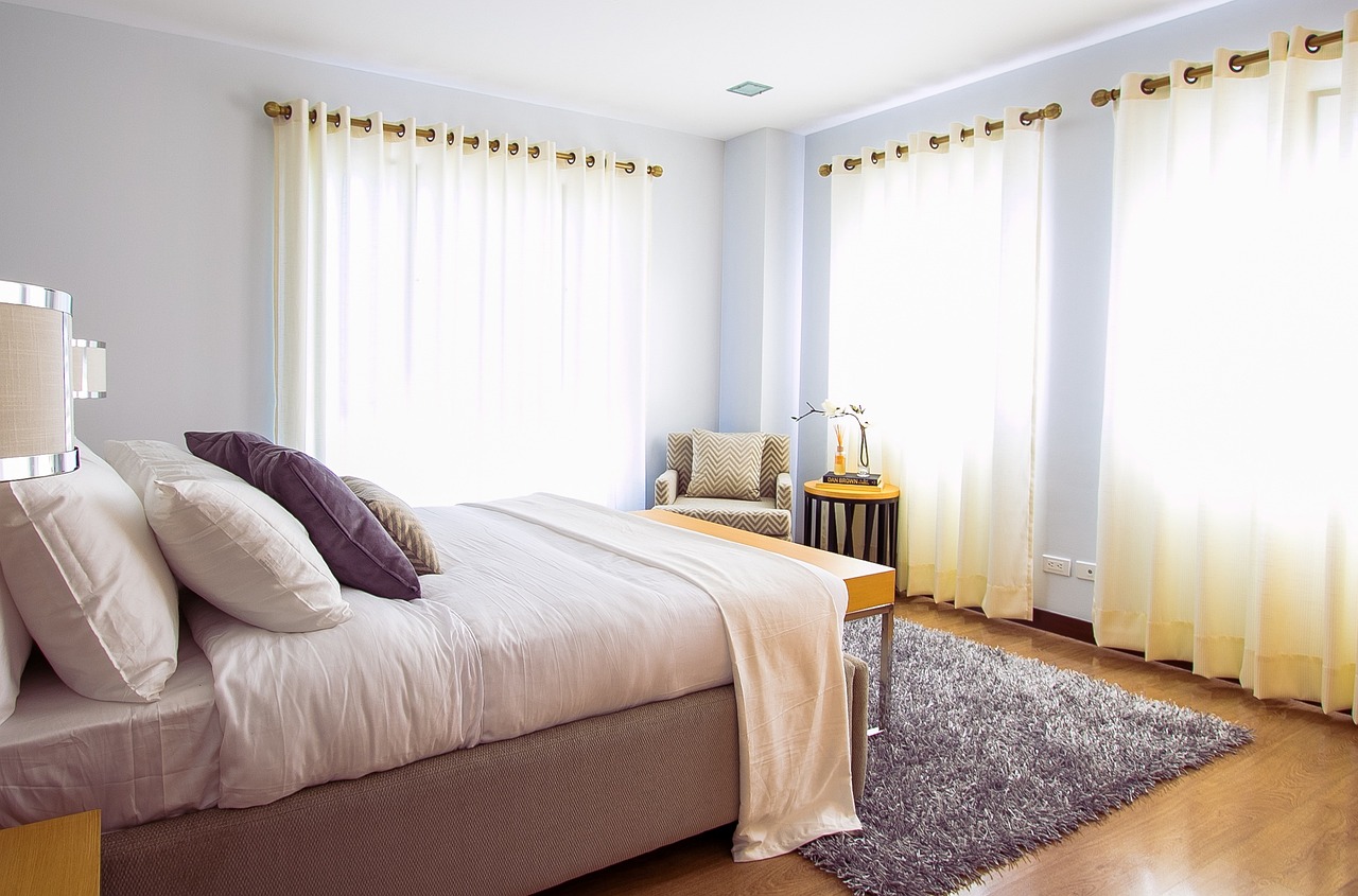 A plush bed made up with cushions and a duvet, with a plush rug and a chair in the corner of the room.
