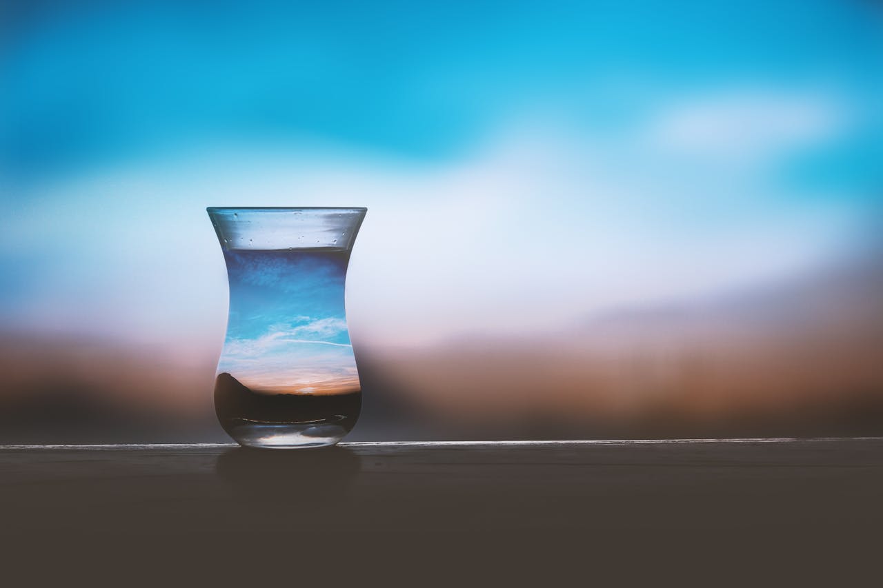 A glass filled with water, with a landscape and sky blurred out in the background, but visible within the water in the glass.