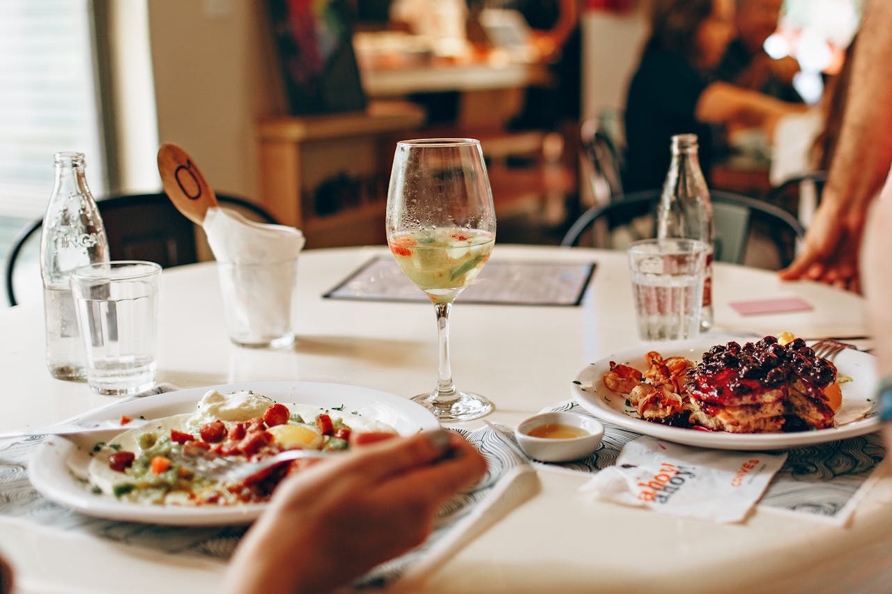 Two plates of food (eggs, and pancakes) next to a glass of wine
