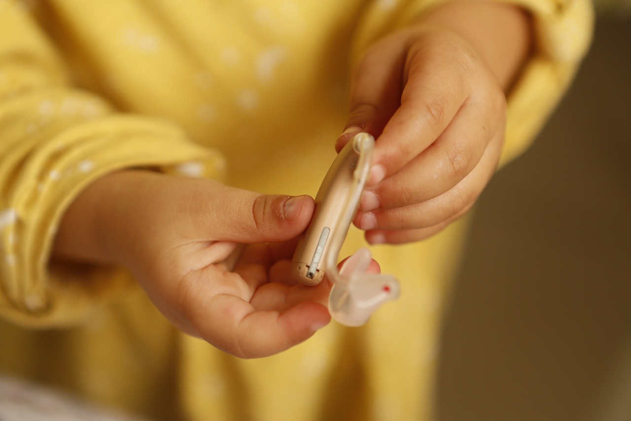 A child wearing yellow, holding a hearing aid.