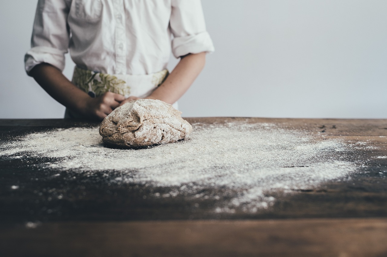 A baker standing behind some dough on a floured work surface.