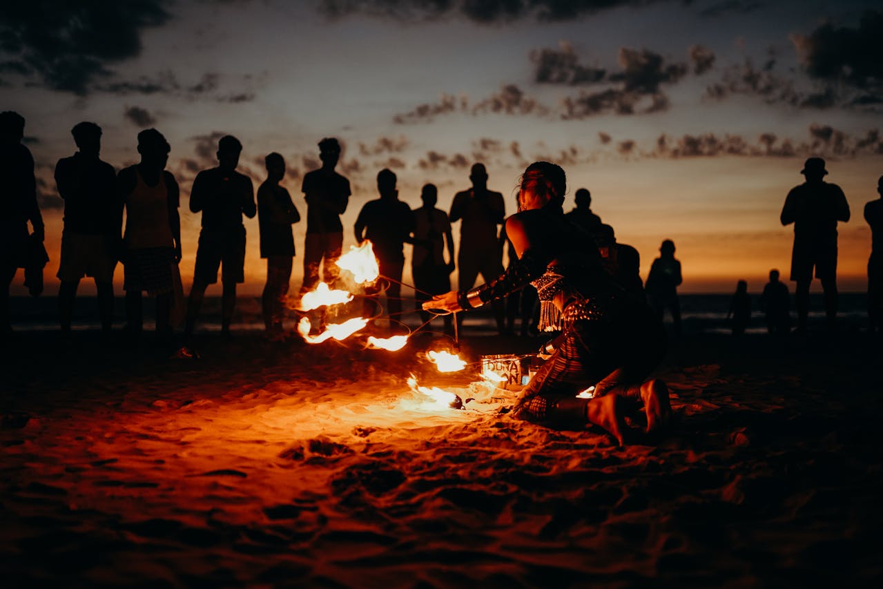 People standing on a beach during sunset, as someone performs with fire in front of them.