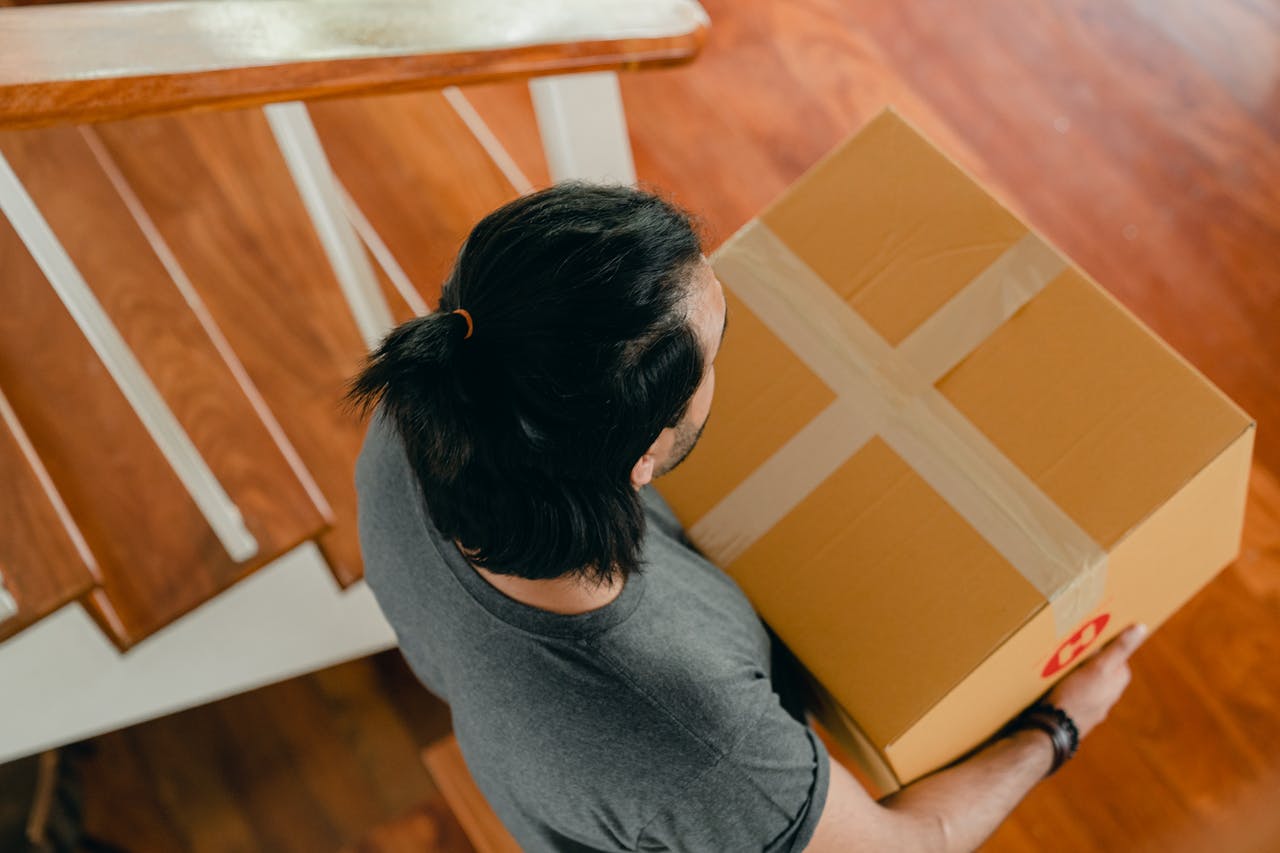 A man carrying a box sealed with masking type down the stairs.