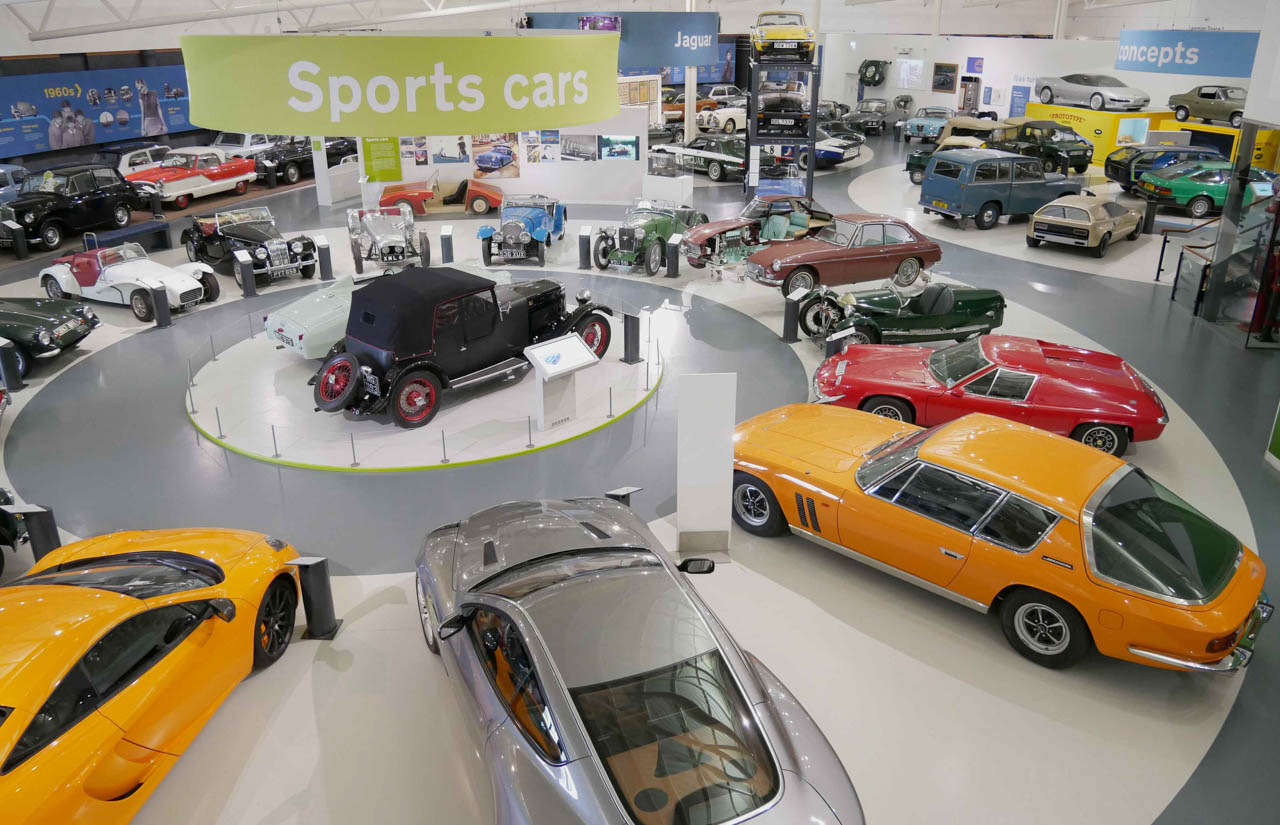 Old sports cars lined up at an exhibition, with a 'sports cars' sign overhead