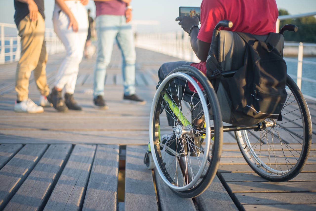 A man sitting in a wheelchair using a tablet, on a boardwalk.